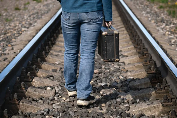 Mujer con una vieja maleta en la mano camina sobre traviesas de un ferrocarril entre rieles — Foto de Stock