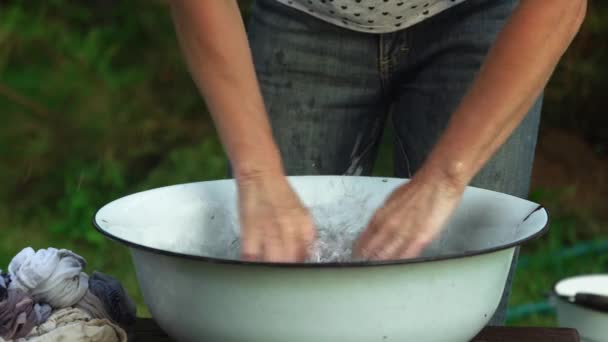 Vrouw spoelt en wikkelt kleding uit met haar handen in het oude bassin buiten op het platteland in de zomer — Stockvideo