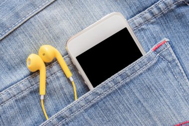 Closeup smartphone ve denim kot pantolon cebinde sarı kulaklık.
