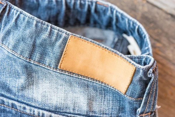 Порожня шкіряна джинсова етикетка на синіх джинсах, дерев'яний фон . — стокове фото