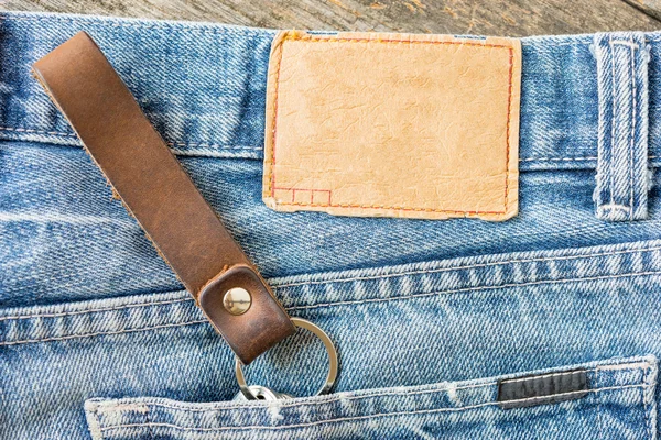 Etichetta di jeans in pelle bianca su un blue jeans, fondo di legno . — Foto Stock