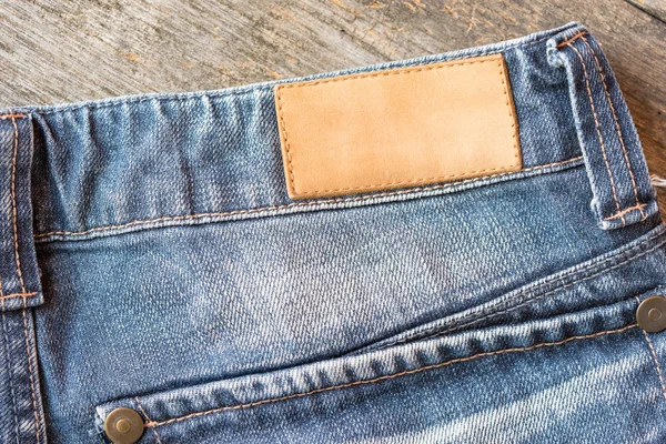 Etichetta in pelle bianca blue jeans su fondo legno . — Foto Stock