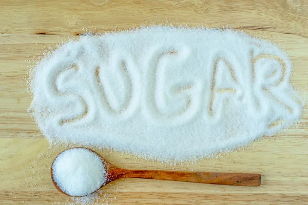 Açúcar de inscrição transformado em pilha de açúcar branco granulado sobre fundo de madeira . — Fotografia de Stock