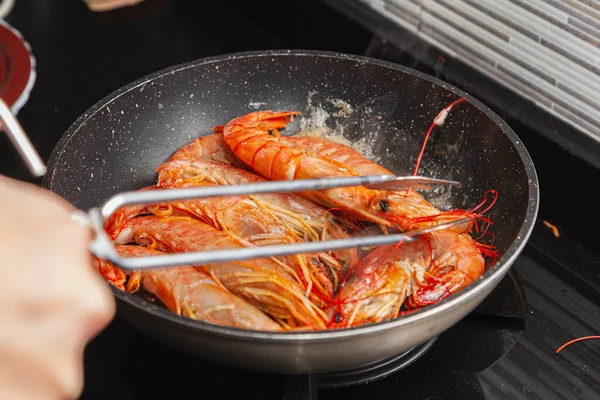 Cooking grilled shrimp in a skillet on a gas stove in the kitchen. Someone is turning them over with kitchen tongs while they are cooking.Prawns being grilled