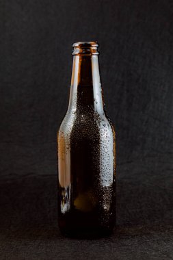 Siyah arka planda yoğunlaşma damlaları olan kahverengi bira şişesi. Şişe açıldı ve metal bir kapağı yok..