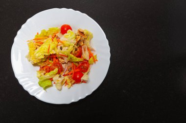 Sebze ve sebzelerin kombinasyonu seramik bir tabakta, mutfakta, karanlık bir bankta. Tarifte marul, kiraz domates, havuç, ceviz, soğan, tohum, aromatik otlar, zeytinyağı ve tuz yer alıyor..