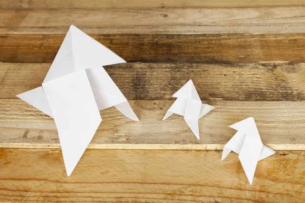 Three classic origami bird figures isolated on wooden background, one of them is bigger and the other two are smaller.