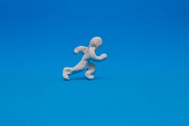 Beyaz plastik bebek mavi arka planda atletizm yapıyor. Bebek yüksek hızda koşuyor Bir yarışta yarışıyor.