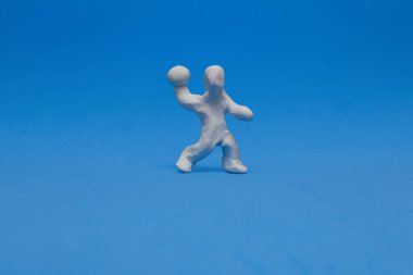 Mavi arka planda Hentbol antrenmanı yapan beyaz bir plastik bebek. Manken topu sağ elinde tutuyor ve atmaya hazır..