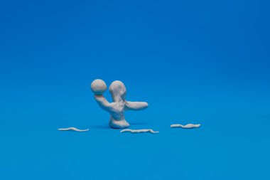 Mavi arka planda su topu oynayan beyaz bir plastik kukla. Manken topu sağ eliyle tutuyor ve fırlatmaya hazır ve etrafında plastikle yapılmış bazı dalgalar var..