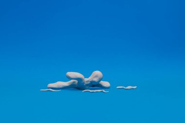 Mavi arka planda yüzme pratiği yapan beyaz bir plastik kukla. Manken yüzüyor ve etrafında plastikten yapılmış dalgalar var..
