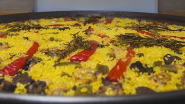 Evde pilav, kırmızı dolma biber, yeşil fasulye, tavuk ve tavşan eti, mantar ve biberiye ile tatlandırılmış diğer bazı malzemelerle pişirilmiş bir paella..
