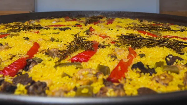 Close-up of a paella cooked at home with rice, red bell pepper, green beans, chicken and rabbit meat, mushrooms and some other ingredients, flavored with a few sprigs of natural rosemary.
