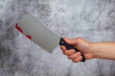 Gri bir arka planda kan lekeleri olan büyük bir kasap bıçağını tutan bir adam..