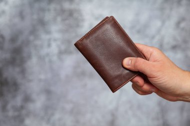 Gri bir arka planda kahverengi deri bir cüzdan tutan bir adam..