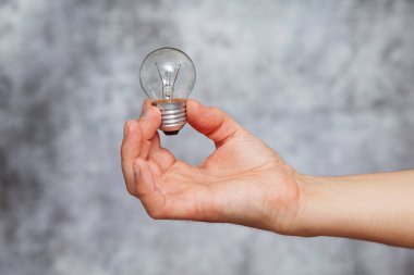 Bir adamın sağ eli solmuş bir tungsten filament ampulü tutarken dokusu gri arka planda.