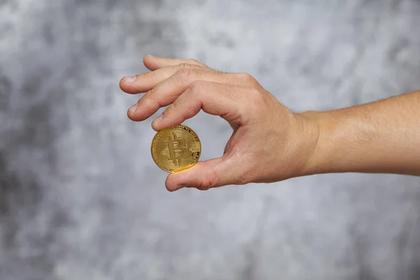 Gri arka planda altın bir Bitcoin tutan bir adamın sağ eli.
