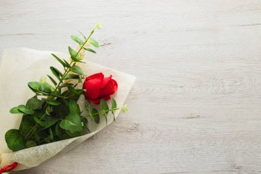 Kırmızı gül beyaz bir kağıtta. Gül beyaz ahşap bir masanın üzerindedir..