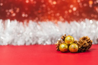 Kırmızı bir yüzey üzerinde Noel altın topları ve çam kozalakları. Gümüş bir çelenk ve karlı kırmızı bir arka plan var..