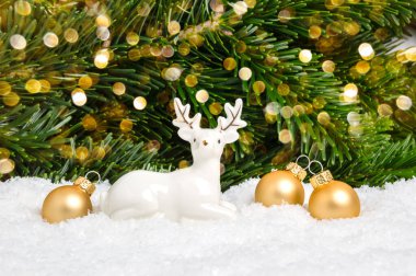 Beyaz Noel geyiği ve arka planda çam ağacı ve bokeh olan altın toplar. Bayramlık tebrik kartı. Mutlu Noeller ve yeni yıl