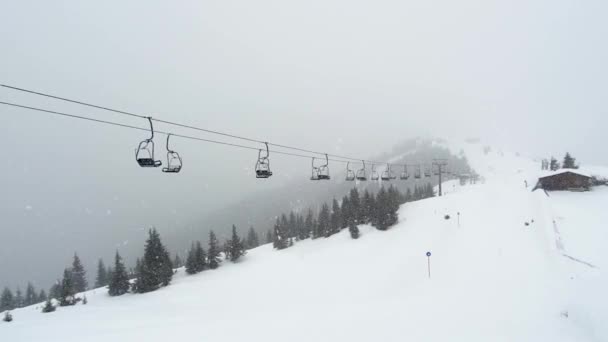 Empty cable car chairlifts move under snow storm in mountains ski resort Zell am See Kaprun, Austria with snowy forest in background. Austrian Alps during bad winter weather with poor visibility — Αρχείο Βίντεο