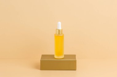 Sarı damlalık serum şişesi ya da altın podyumda duran bej arkaplanlı yağ. C vitamini ile organik cilt bakımı kozmetikleri, sağlık, kaplıca ve güzellik tedavi konsepti, ürün modeli