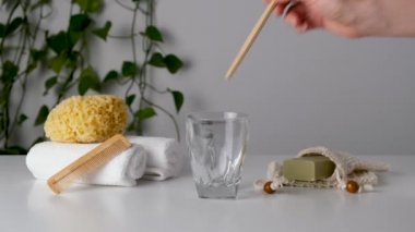 Kadın eli bambu diş fırçasını çevre dostu banyo aksesuarları arasına koyar: doğal deniz süngeri, organik tasarruf torbası sabunu, ahşap tarak. Sıfır atık spa ve banyo ürünleri. Doğal cilt bakımı