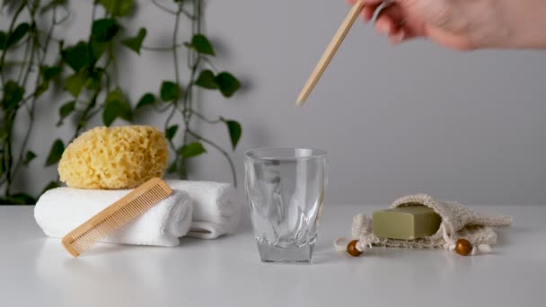 Mano de mujer pone cepillo de dientes de bambú en vidrio entre los accesorios de baño ecológicos: esponja de mar natural, jabón en bolsa de ahorro orgánico, peine de madera. Cero residuos de spa y productos de baño. Cuidado natural de la piel — Vídeos de Stock