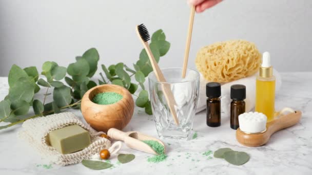 Femme main met brosses à dents en bambou dans le verre parmi les accessoires de salle de bain respectueux de l'environnement : huile essentielle d'eucalyptus, sels de bain, éponge de mer, savon dans un sac économiseur. Produits de spa et de bain zéro déchet — Video