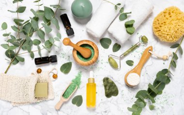 Doğal cilt bakımı ve okaliptüslü aromaterapi gerekli yağ şişeleri, banyo tuzu, güzellik yeşimi silindiri, mermer arka planda gua sha. Spa, sağlık, masaj ve rahatlama konsepti. Üst manzara, düz uzanma