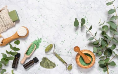 Doğal cilt bakımı ve okaliptüslü aromaterapi esaslı yağ şişesi, banyo tuzu, güzellik yeşimi silindiri, mermer arka planda gua sha. Spa, sağlık, masaj, rahatlama konsepti. Üst görünüm, alanı kopyala