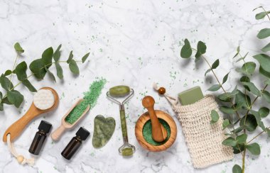 Doğal cilt bakımı ve okaliptüslü aromaterapi esaslı yağ şişesi, banyo tuzu, güzellik yeşimi silindiri, mermer arka planda gua sha. Spa, sağlık, masaj, rahatlama konsepti. Üst görünüm, alanı kopyala