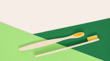 Geometrik bej ve yeşil arka planda çevre dostu bambu diş fırçası. Plastiksiz diş bakımı ürünü olarak iki doğal ahşap diş fırçası. Sıfır atık, sürdürülebilir yaşam tarzı. Düz yatış, üst görünüm