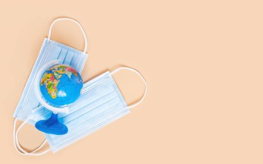 Tarafsız bej arka planda küresel ve tıbbi maskeler ve metin için fotokopi alanı. Küresel koronavirüs ya da Covid-19 salgınından kaynaklanan minimum küresel hastalık yayılımı, seyahat kısıtlamaları