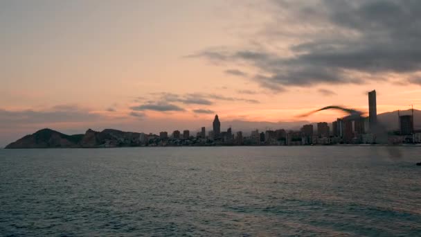 Belo pôr do sol sobre Benidorm e praia de Poniente, Espanha. Skyline com arranha-céus, edifícios da cidade, montanhas e céu vermelho. Gaivota a voar para a câmara. Ondas de mar calmas. Região bela Costa Blanca — Vídeo de Stock