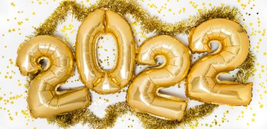 Altın 2022 balon. Mutlu Yıllar kutlamaları için altın metalik folyo numaraları beyaz arka planda parlayan konfeti yıldızları ve çelenklerle birlikte. Tatil partisi dekorasyonu veya kartpostal pankartı konsepti