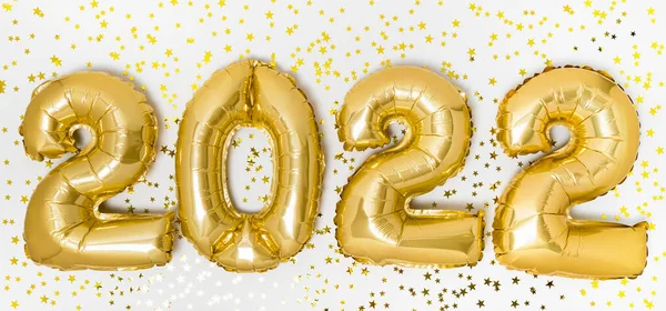 Golden 2022 balloons. Gold metallic foil numbers for Happy New Year celebration on white background with glitter confetti stars. Helium balloon as holiday party decoration or postcard banner concept
