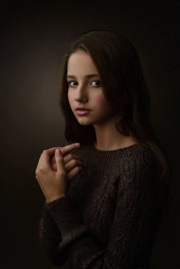 Kahverengi arka planda kahverengi kazaklı bir kızın portresi.