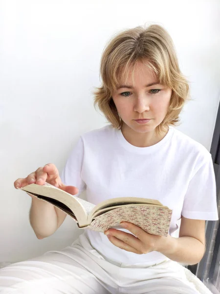 Atrakcyjna blondynka siedząca na parapecie i czytająca książkę — Zdjęcie stockowe
