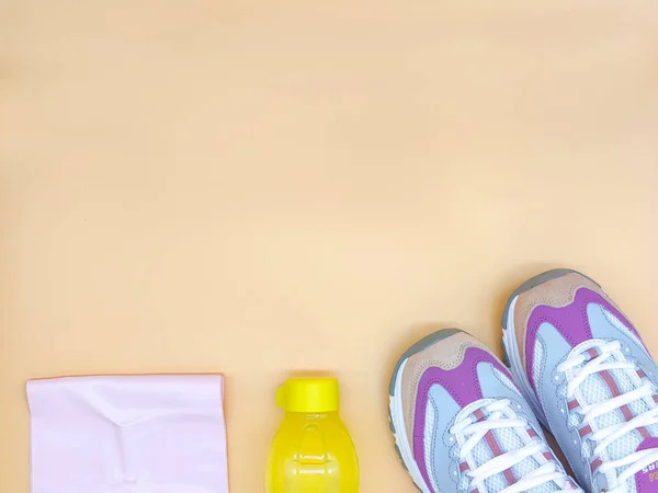 Set stylish sneakers, fitness rubber band stretch, yellow bottle on the beige background, fitness concept, copy space