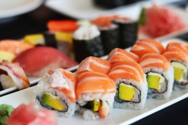 Avokado ve suşi kombinasyonlu yuvarlaklar dikdörtgen beyaz plakalar üzerinde koyu arkaplan üzerinde