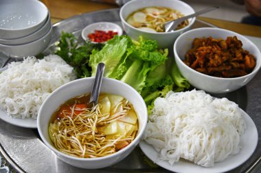 Yuvarlak tepside Vietnam yemeği, beyaz tabaklar, pirinç eriştesi, soya lahanalı sos, marul yaprağı.