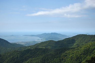 Adanın ve denizin tepe manzarası güneş, ağaçlar ve yeşilliklerle aydınlanıyor.
