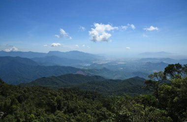 Dağdan vadiye, güneşle aydınlatılan bir şehir, bulutların altında bir sürü ağaç ve yeşillik var.