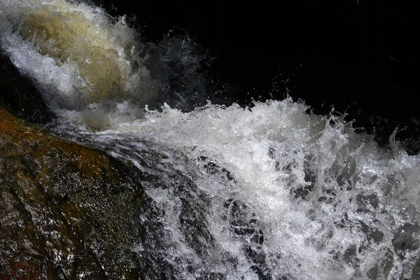 渓流は石の上を流れ 暗い背景に光が飛び散る — ストック写真
