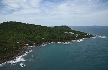Deniz, kıyı şeridi ve adanın sonu, tepeler, taşlar, orman ve balıkçı evleri, üst manzara, beyaz deniz köpüğü.