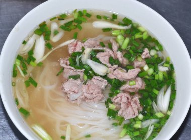 Vietnam pho bo çorbası sığır eti, pirinç eriştesi ve soğanlı, beyaz tabakta, üst manzara, yakın çekim.