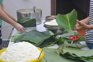 Bir adam ve bir kadın Vietnam 'ın yeni yılı için pirinç, domuz, bezelye ve muz yapraklarına sarılmış Banh Chung keki hazırlıyorlar.
