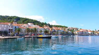Korcula sahilinin panoramik manzarası. Limanda dağlar, evler ve tekneler var.