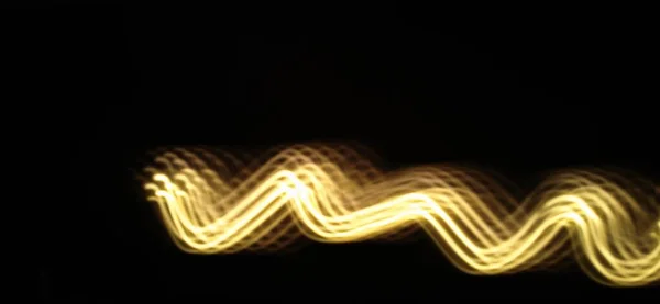 Closeup of Glowing Neon yellow wave pattern abstract flowing through the isolated black background with copy space. Using light painting technique